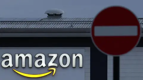 Getty Images Una foto de 2023, que es un primer plano de un cartel con el logotipo de Amazon en un almacén de Amazon en Coventry. Delante de la fábrica se ve una señal de stop roja.
