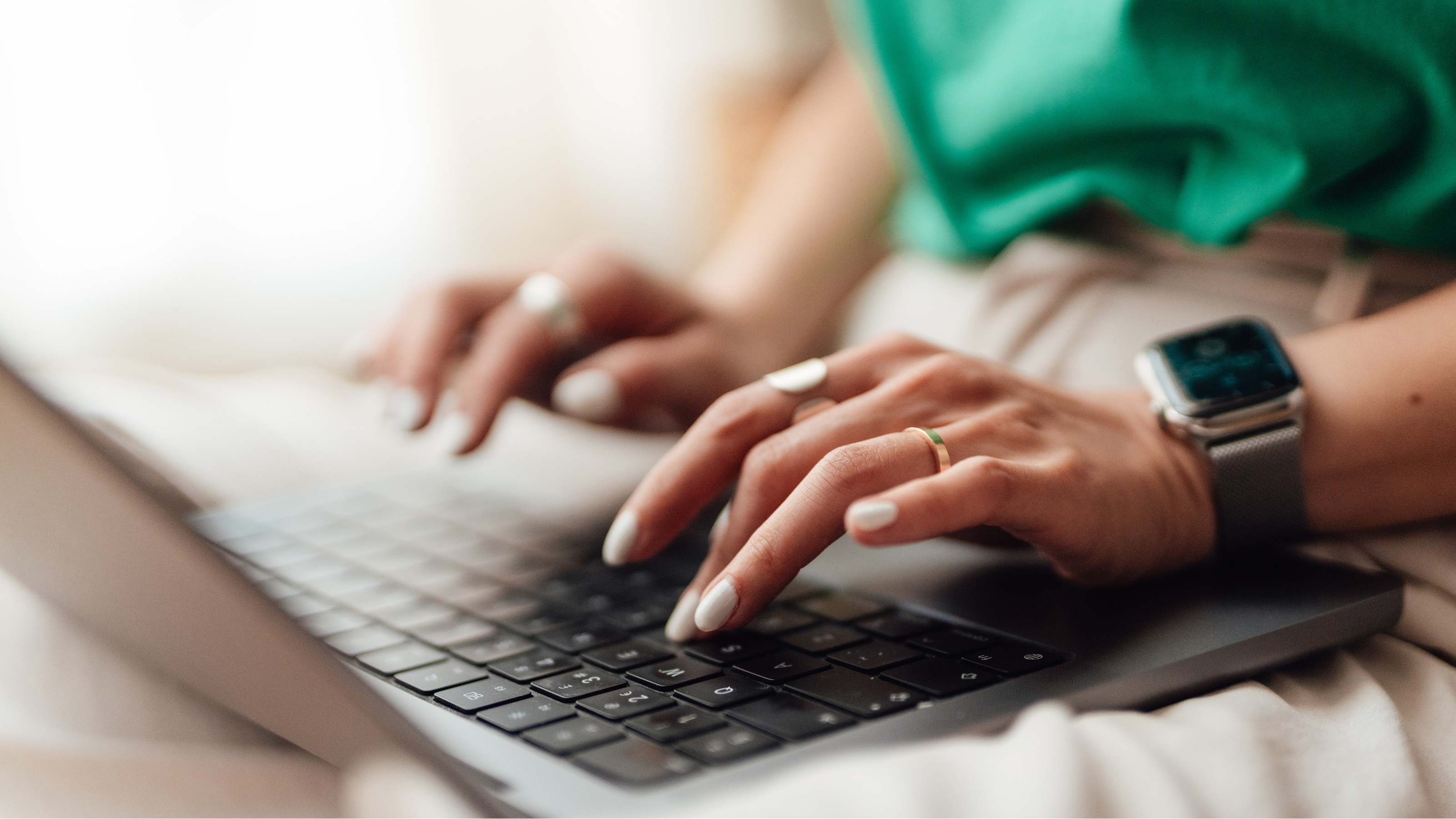 Una mujer está escribiendo en una computadora portátil, solo se muestran sus manos.