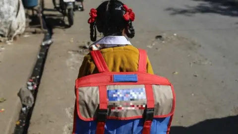Getty Images Una vista posterior de una niña, vestida con uniforme escolar y cargando una mochila, caminando por una calle de la India.